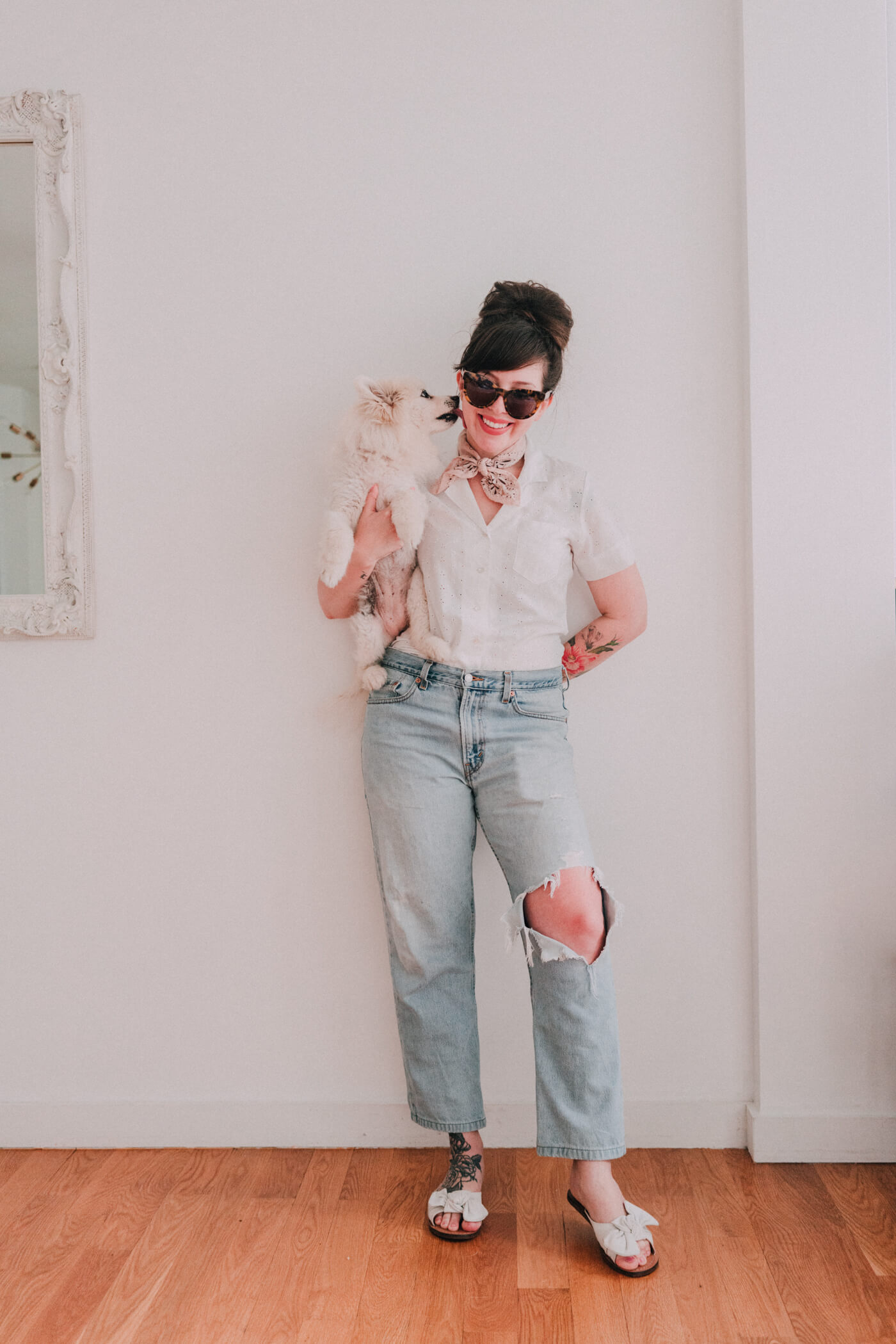 woman wearing white shirt and tattered jeans and carrying her dog