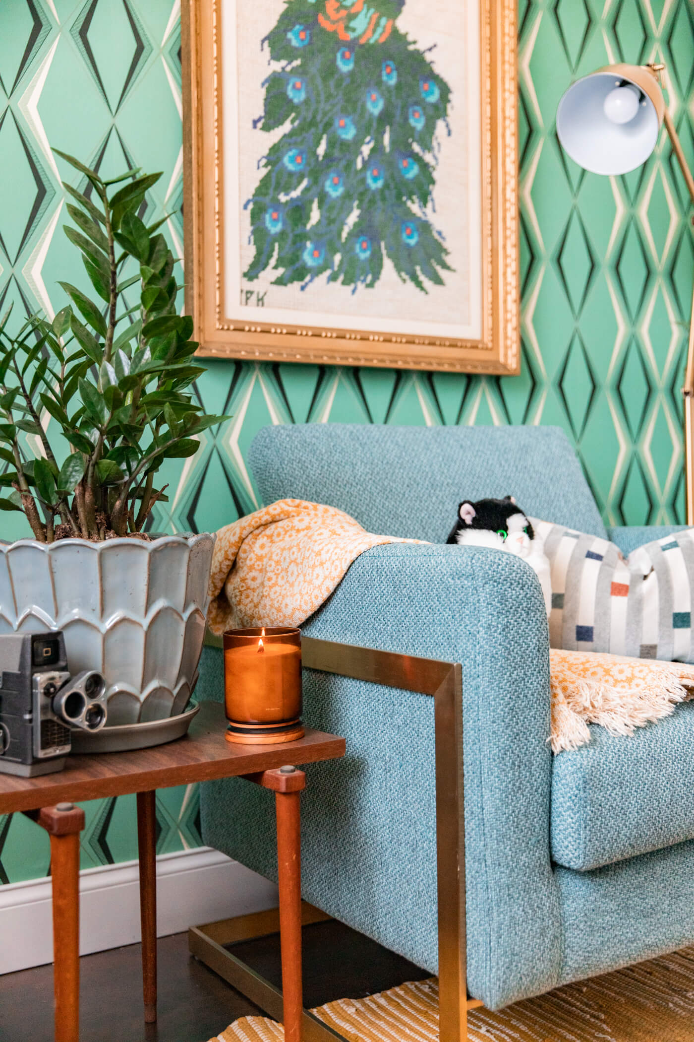 blanket, stuffed animal and pillow on a blue chair, lit candle, vintage camera, and plant on a side table for HomeGoods Home Office Makeover