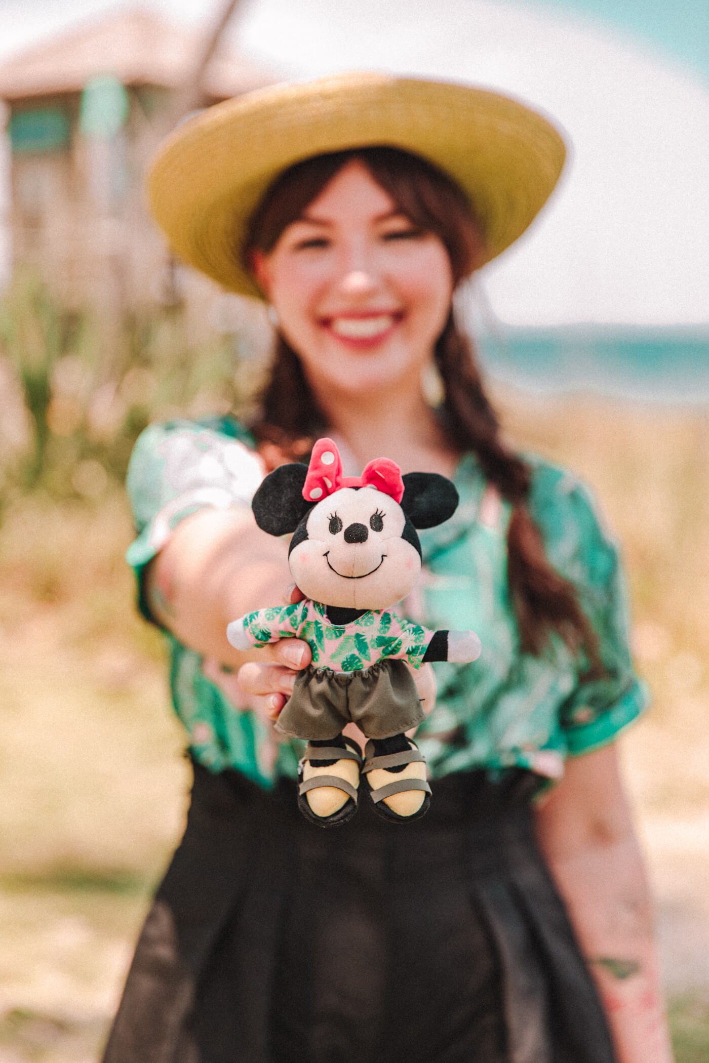 woman wearing green top and black shorts and holding out a mouse stuffed toy