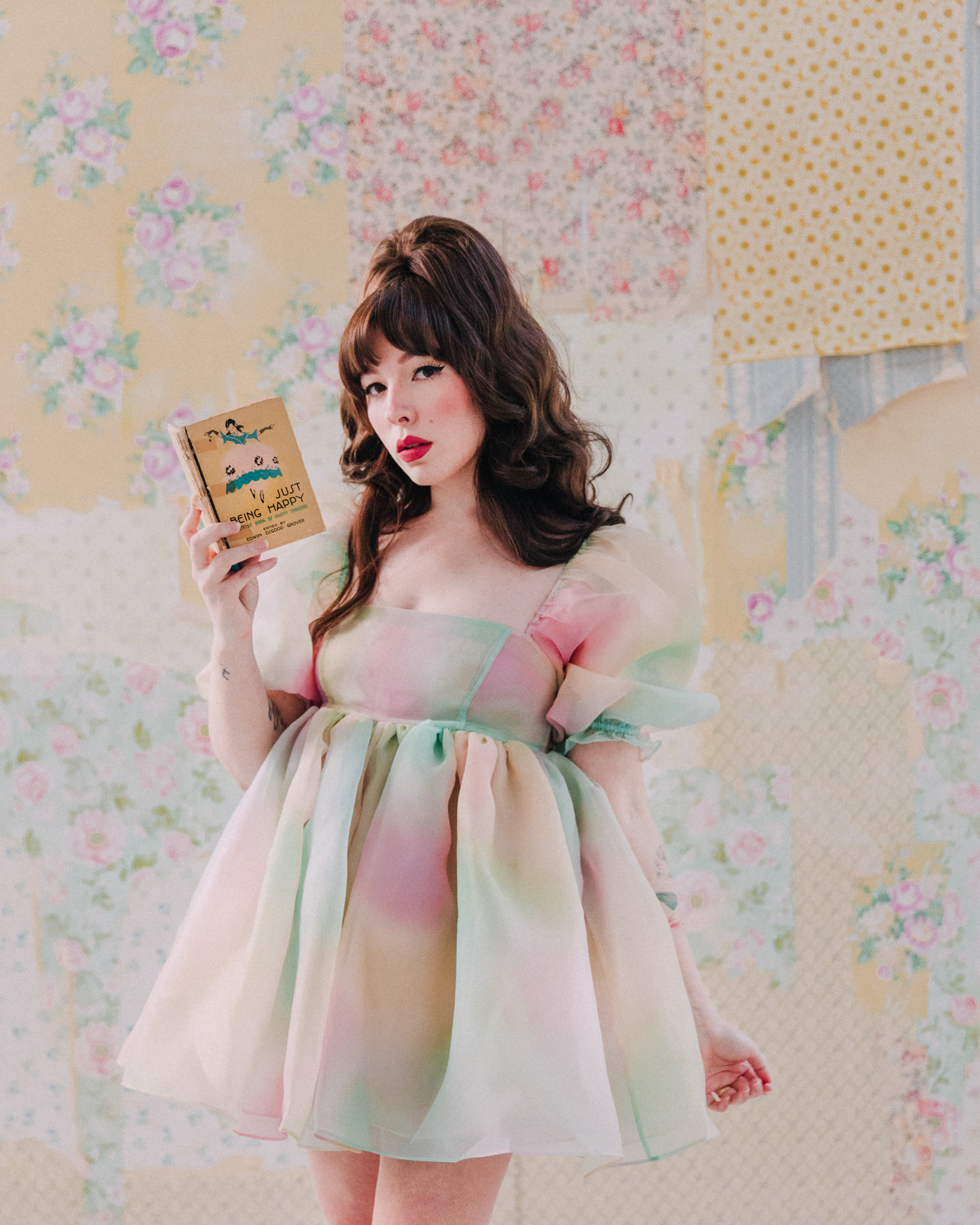 woman wearing rainbow dress, red lipstick, and signature eye makeup and holding a book