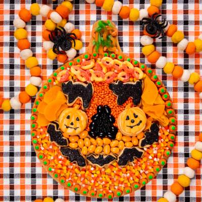 wooden snack board with assorted orange and black snacks assembled to resemble a pumpkin