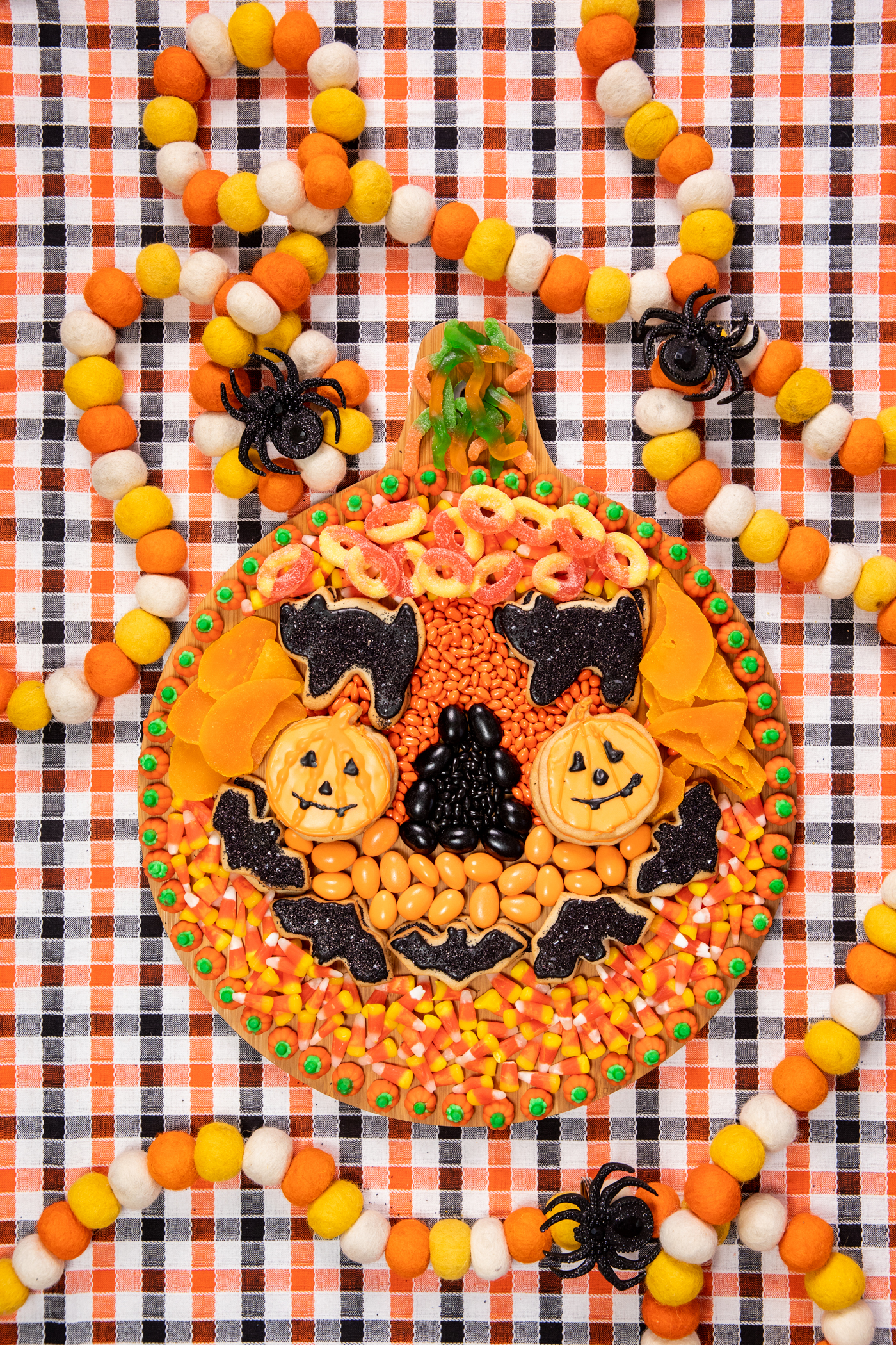 wooden halloween snack board with assorted orange and black snacks assembled to resemble a pumpkin