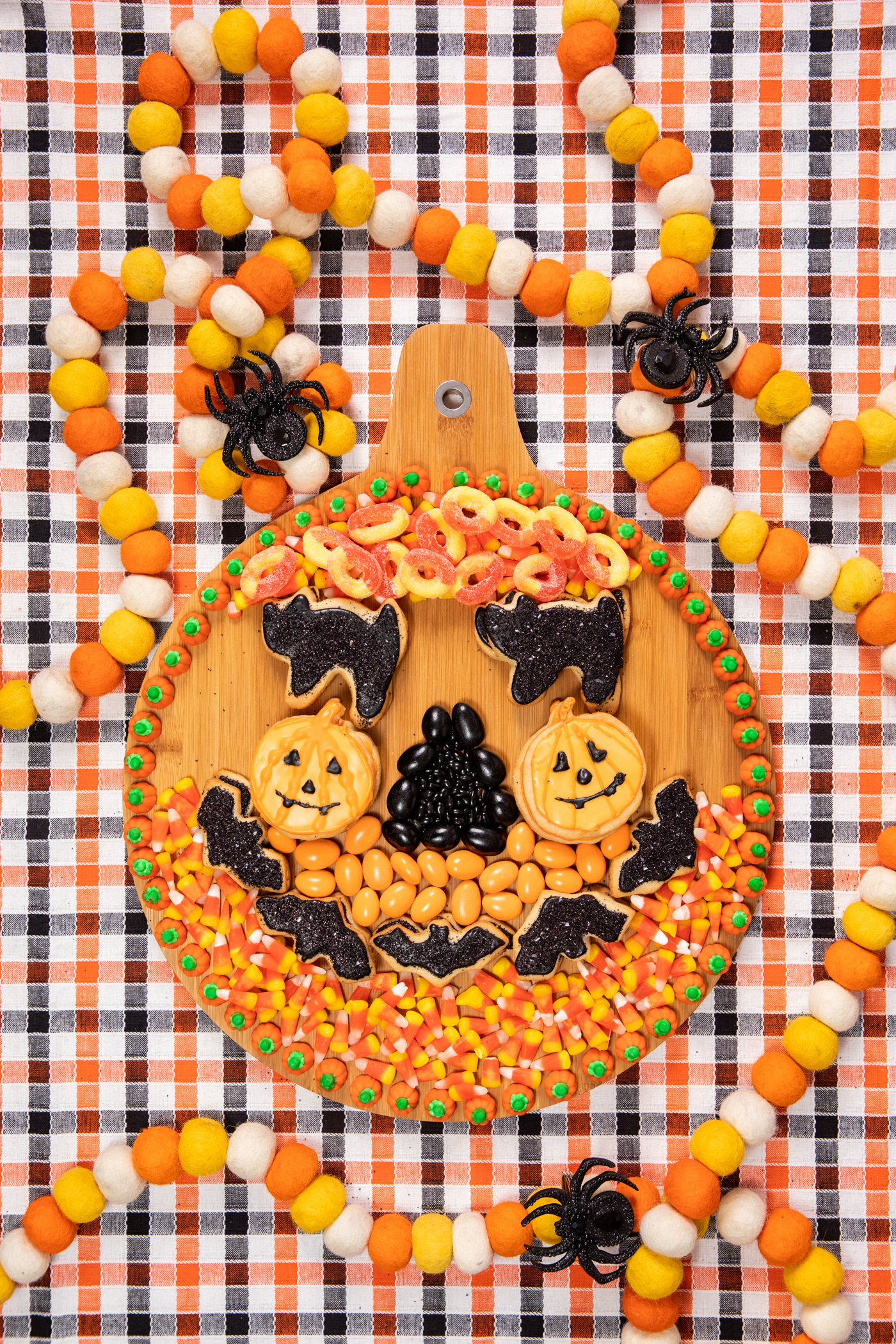 wooden halloween snack board with assorted orange and black snacks assembled to resemble a pumpkin