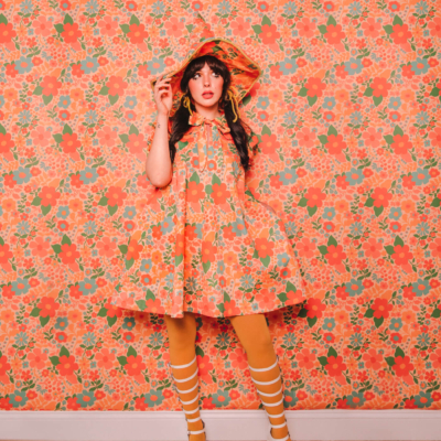 Evelyn Bourdon wearing a handmade dress and matching witch hat made out of Spoonflower fabric, in front of matching wallpaper in the same print.