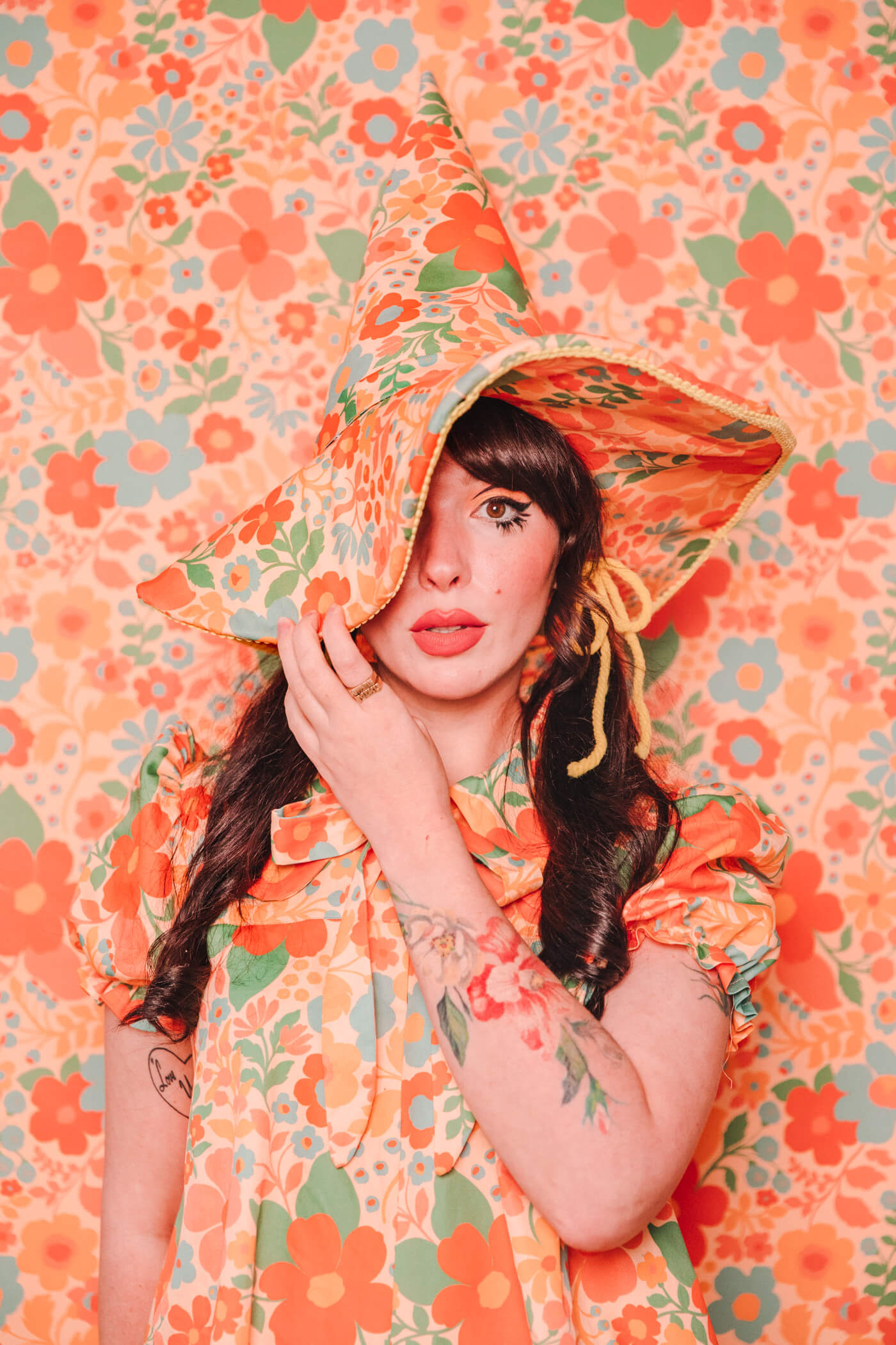 Evelyn Bourdon wearing a handmade dress and matching witch hat made out of Spoonflower fabric, in front of matching wallpaper in the same print.