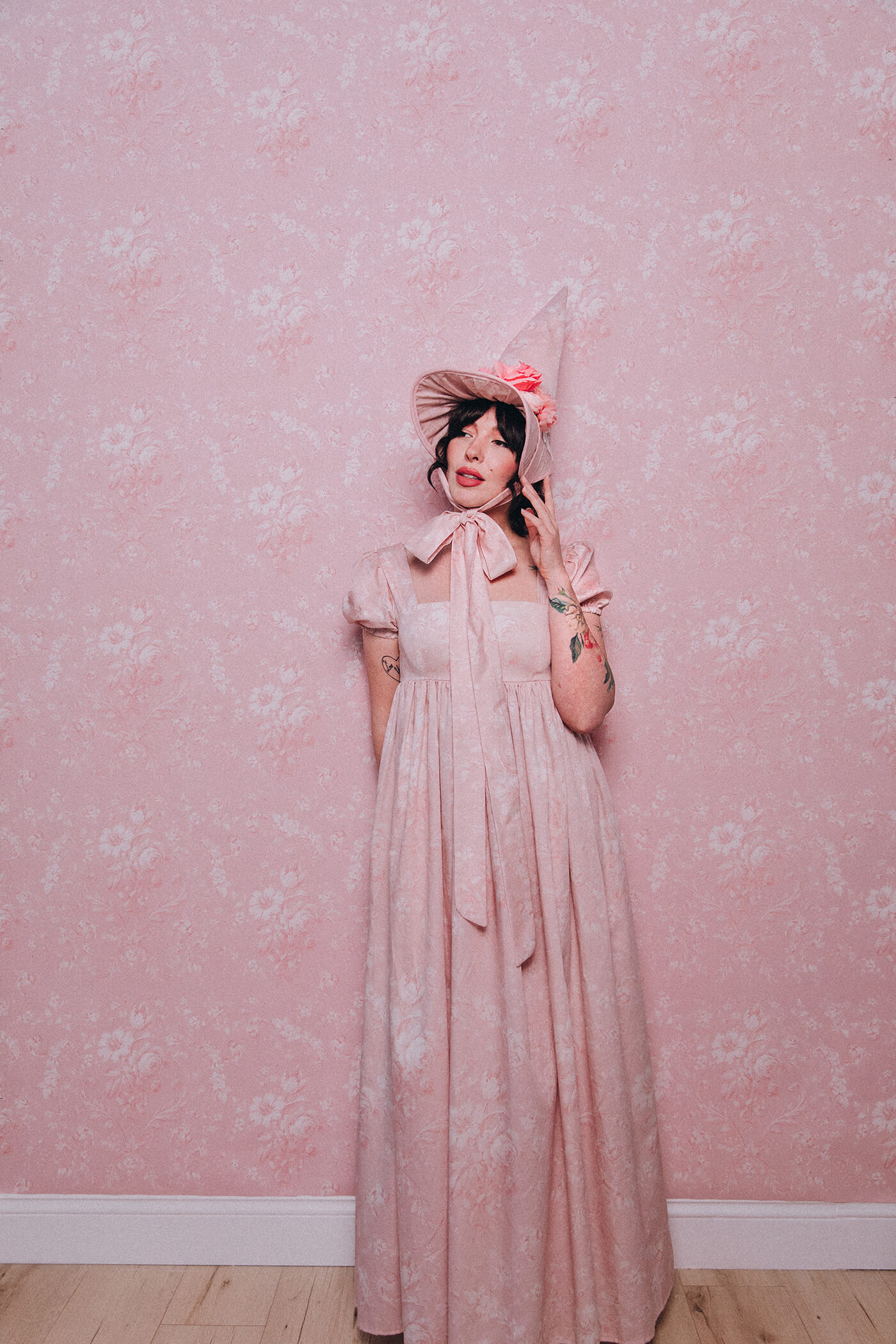 Evelyn Bourdon wearing a handmade dress and matching witch hat made out of Spoonflower fabric, in front of matching wallpaper in the same print.