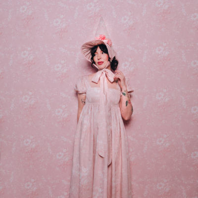 Evelyn Bourdon wearing a handmade dress and matching witch hat made out of Spoonflower fabric, in front of matching wallpaper in the same print.