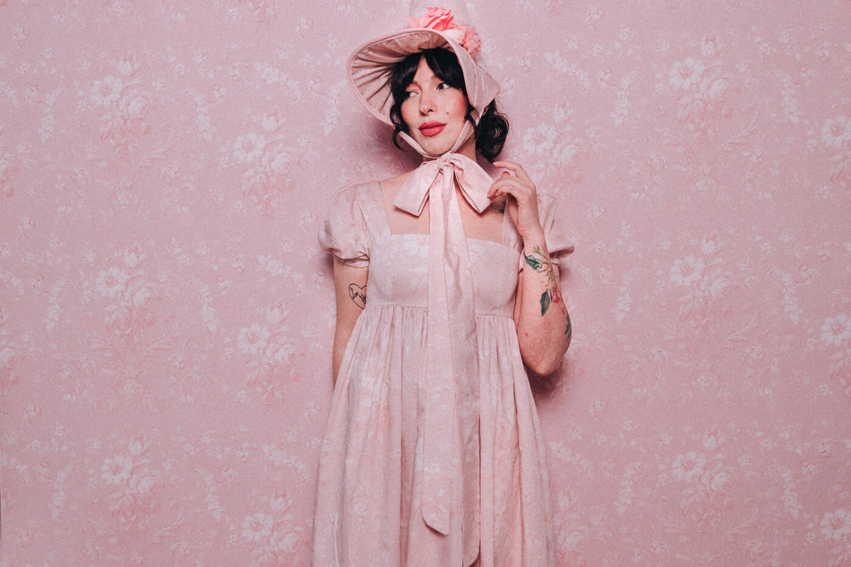 Evelyn Bourdon wearing a handmade dress and matching witch hat made out of Spoonflower fabric, in front of matching wallpaper in the same print.