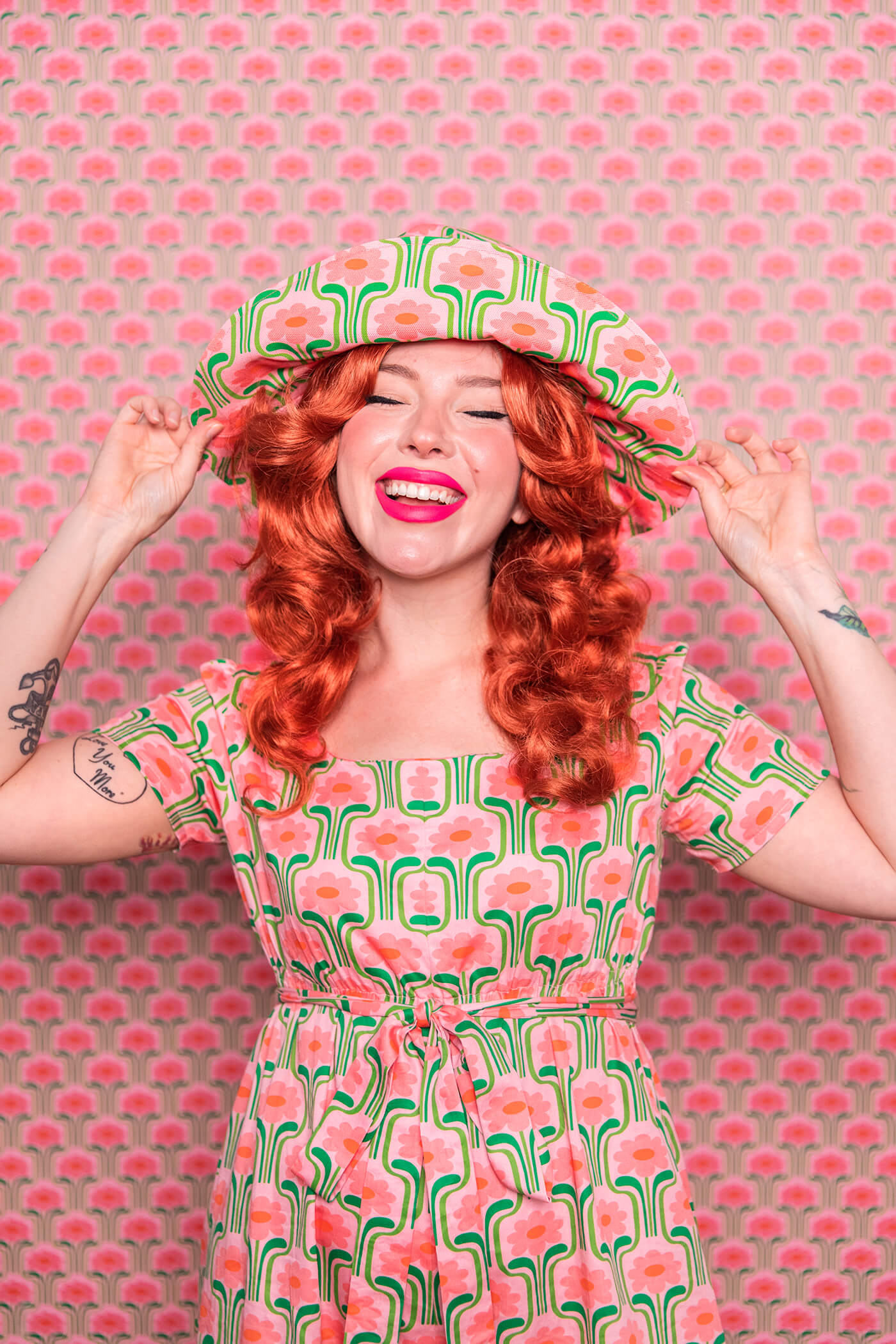 Evelyn Bourdon wearing a handmade dress and matching reversible bucket and witch hat made out of Spoonflower fabric, in front of matching wallpaper in the same print.